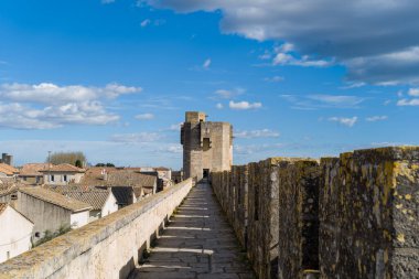 Antik surların tepesindeki uzun taş geçitler orta çağ kare bir kuleye çıkıyor. Terracotta çatılarına bakıyor. Parlak mavi gökyüzünün altında Aigues-Mortes 'de dağınık bulutlar var..