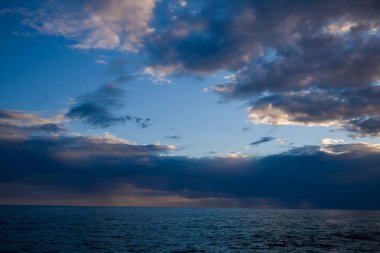 Sakin bir deniz manzarası, Adriyatik Denizi 'ni alacakaranlıkta katmanlı bulutlarla dolu dramatik bir gökyüzünün altında gösteriyor. Mavi ve nazik ışığın ince gradyanı barışçıl ve açık bir ufuk yaratır..