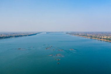 Stoeng Treng, Kamboçya yakınlarındaki Mekong Nehri 'nin engin hava manzarası, ufka doğru uzanan sakin mavi su ve yüzeyin altında görünen dağınık adacıklar. Nehir kıyıları kuru ormanlık ve uzak yerleşim yerleriyle doludur.