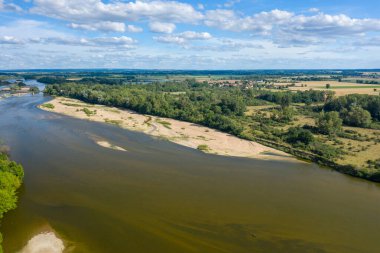 Loire Nehri 'nin geniş kumlu kıyıları, yoğun yeşil ormanı ve Pouilly sur Loire yakınlarında açık kırsal manzarası kümülüs bulutlarıyla kaplı bir gökyüzünün altında. Sahne, huzurlu bir yaz atmosferi ve doğal dokuları yansıtıyor..