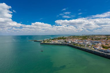 Ile de Re, Charente-Maritime 'in liman ve beyazlatılmış evleri, turkuaz Atlantik suları ve dağınık bulutlarla dolu bir gökyüzü ile çevrili geniş bir hava manzarası. Görüntü adaların sahil cazibesini, marinasını ve sakin sahil kenarını vurguluyor.
