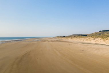 Plage de la Vieille eglise 'de geniş kumlu kıyı şeridi boyunca uzanır. Açık mavi gökyüzü ve yumuşak ışık açık, huzurlu bir sahil atmosferi yaratır..