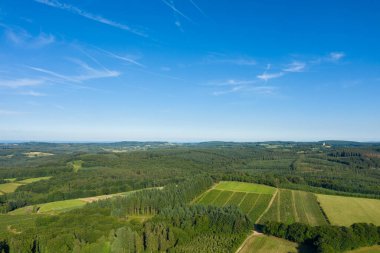 Hava manzarası, Morvan bölgesinde geniş bir yeşil alan ve yoğun ormanlık alanı gösteriyor. Sahne açık mavi gökyüzünün altında parlak güneş ışığıyla yıkanır, yuvarlanan araziyi ve doğal dokuları vurgular..