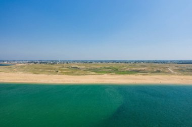 Engin kumlu kıyı şeridi, Brittany 'deki Barre dEtel' de bulutsuz mavi gökyüzünün altında berrak bir turkuaz denizle buluşuyor. Doğal dokular ve uzak yeşilliklerle manzara açık ve huzurlu görünüyor..