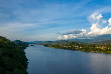 Luang Prabang şehrinin geniş manzarası yemyeşil tepeler ve büyük Mekong nehri arasında dramatik bulutların altında. Sahne tropikal bitki örtüsü, uzak dağ sıraları ve kuzey Laos 'taki sakin suyu vurguluyor..