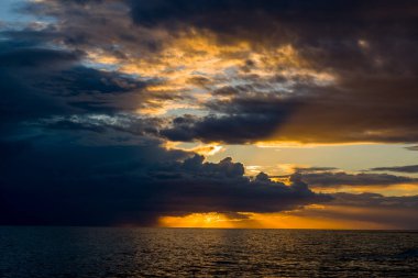Adriyatik Denizi 'nin yukarısındaki dramatik fırtına bulutlarından geçen parlak altın güneş ışığı, su boyunca cesur ışınlar ve yansımalar oluşturur. Sahne, karanlık gökyüzünün çarpıcı bir etkileşimini ve gün batımında aydınlanan ufku gösteriyor..
