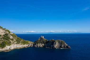 İtalya 'daki engebeli Capo di Conca' nın tepesinde, yemyeşil Akdeniz bitki örtüsü ve derin mavi sularla çevrili, ıssız bir sahil gözetleme kulesi bulunur. Amalfi Sahili 'nin dramatik kıyı şeridi açık gökyüzü ve uzak gökyüzü tarafından çevrelenmiştir.