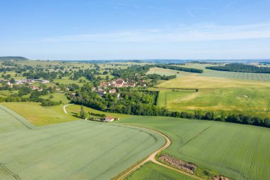 Bereketli tarım arazileri, dolambaçlı yollar ve açık mavi gökyüzünün altındaki geniş yeşil alanlarla çevrili Cuncy les Varzy köyünün havadan görünüşü..
