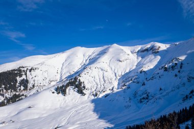 Mont Jolys 'in karla kaplı yamaçlarının engin manzarası. Dağınık yeşil ağaçlar ve derin gölgeler. Açık mavi gökyüzü ve kışın hafif olması çarpıcı bir dağ manzarası yaratır..