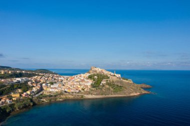 Castelsardos 'un insansız hava aracı perspektifi Akdeniz kıyı şeridi üzerinde yükselen renkli binalar ve açık mavi gökyüzü altında bir ortaçağ kalesi..