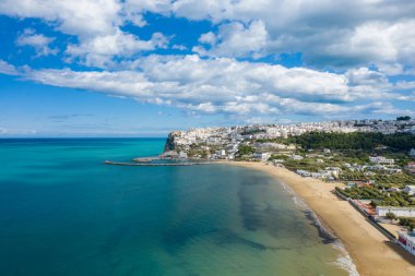 Peschicis 'in yüksek açılı manzarası altın plajı süpürüyor canlı turkuaz körfez boyunca kıvrılıyor, burnun altında çarpıcı bulutlarla dolu beyaz binalar yığılıyor..