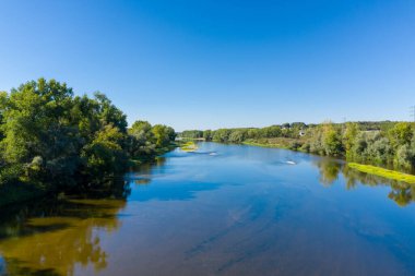 Yoğun yeşil ağaçlar ve kumlu arazilerle çevrili geniş nehir, Fransa 'nın orta kesimindeki Imphy yakınlarında açık mavi bir gökyüzünün altından akar. Sakin manzarada sakin su, yemyeşil yeşillik ve doğal yansımalar bulunur..