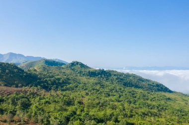 Dien Bien, Vietnam 'da canlı yeşil bir tepe beyaz bulutlar denizinin üzerinde yükseliyor. Açık mavi gökyüzü ve uzak tepeler taze, açık bir manzara yaratır..