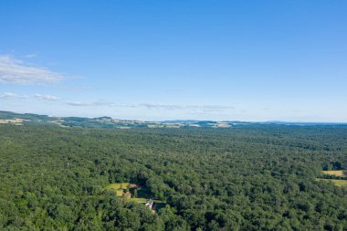 Morvan bölgesinde geniş, açık mavi gökyüzünün altında dağınık açıklıklar ve kayan tepelerle yoğun yeşil ormanlık bir alan. Görüntü sükuneti, doğal dokuları ve yaz kırsalının ölçeğini aktarıyor..