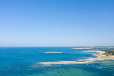 Saint Philibert yakınlarında, bulutsuz mavi gökyüzünün altında, orman ve uzak kıyı şeridi ile çevrili, görünen kumsalları ve berrak turkuaz suyu ile geniş bir hava manzarası..