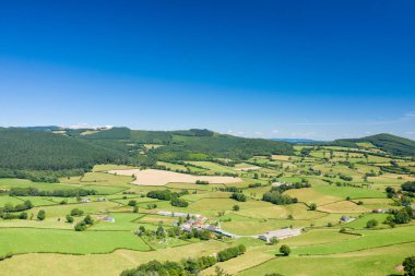 Morvan bölgesindeki canlı mavi gökyüzü altında yama işleri tarlalarının ve yeşil yuvarlanan tepelerin havadan görüntüsü. Manzara yemyeşil, açık ve küçük kırsal binalarla benekli..
