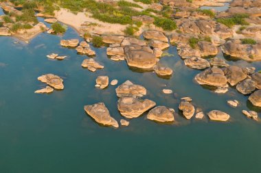 Güney Laos 'un Champassak kenti yakınlarındaki Mekong Nehri boyunca sığ mavi-yeşil sular ve kumlu kıyılara dağılmış pürüzsüz kumtaşı oluşumlarının hava perspektifi. Sıcak gün ışığı doğal desenleri, ince dokuları ve seyrek yeşilliği vurgular.