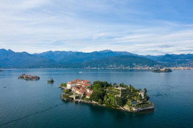 Isola Bella 'nın süslü teras bahçeleri ve Maggiore Gölü' nün mavi sularıyla çevrili tarihi sarayı geniş hava perspektifi. Sahne uzak dağları, göl kentleri ve zarafeti yansıtan sakin bir gökyüzünü içeriyor.