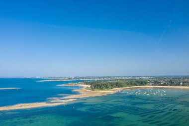 Saint Philibert yakınlarındaki şeffaf turkuaz suyun altında kumlu baraların ve geometrik istiridye yataklarının havadan görünüşü, orman yarımadası ve kıyı şeridi boyunca canlı mavi bir gökyüzünün altında bulunan tekneler..