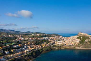 Castelsardos 'un geniş hava manzaralı modern yerleşim alanı engebeli kıyı şeridi boyunca uzanan pastel binalar, yuvarlanan tepeler ve berrak mavi gökyüzünün altında görünen tarihi kale..