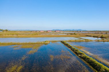 Kamboçya, Kamboçya yakınlarındaki düzlük boyunca genişleyen tuz buharlaşma göletleri canlı mavi gökyüzünü yansıtıyor. Kırmızı çatılı tuz depoları ve uzak tepeler sakin kırsal alanı tamamlıyor..