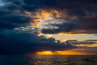 Adriyatik Denizi 'ni silip süpüren kara fırtına bulutları ufuktaki parlak altın güneş ışığını aydınlatıyor. Sahne, aydınlık gökyüzü ve gölgeli su arasında çarpıcı bir kıyı manzarası oluşturan çarpıcı zıtlıklar içeriyor..
