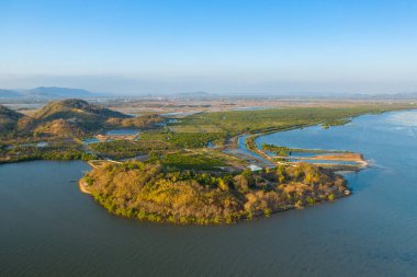 Havadan bakıldığında, sakin nehir sularıyla çevrili ve Kamboçya, Kamboçya yakınlarındaki yemyeşil sularla çevrili güneşli bir yarımada görülüyor. Manzarada geometrik balık göletleri, yeşil bitki örtüsü ve açık mavi gökyüzünün altındaki uzak tepeler yer alır.