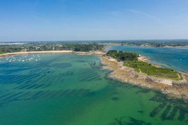 Zümrüt suyla çevrili kayalık bir yarımadanın insansız hava aracı görüntüsü ve açık mavi gökyüzünün altında Anse de Trehennarvour, Saint Philibert yakınlarındaki görülebilir istiridye yatakları..