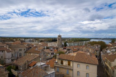Tarihi bir taş kulesi ve Rhone Nehri 'nin dramatik, bulutlarla dolu gökyüzünün altında dalgalandığı Arles' in terasotta çatılarının geniş manzarası..