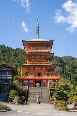 Japonya 'nın Wakayama kentinde Kumano Nachi Taisha' da, açık mavi bir gökyüzünün altında, manikürlü çalılar ve yemyeşil orman tepeleriyle çerçevelenmiş, üç katlı geniş bir taş merdivenin tepesinde duruyor. Kıtır güneş ışığı canlı renkleri yükseltir ve...