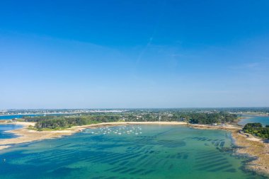Geometrik istiridye yataklarının ve turkuaz sularda demirlemiş teknelerin hava perspektifi Anse de Trehennarvour, Saint Philibert yakınlarındaki yeşil ormanla çevrili kumlu bir sahil şeridi boyunca canlı mavi gökyüzü altında..