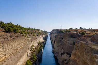 Dikey kireçtaşı duvarlar dar Corinth Kanalı 'nı sarar, mavi su engebeli araziyi keser ve parlak, bulutsuz bir gökyüzünün altında yeşil alana yayılır..