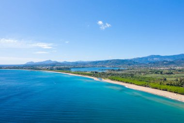 Sardinya, Lotzorai yakınlarında canlı turkuaz suyu ve yemyeşil kıyı şeridi olan geniş kumlu bir sahil. Sahnede uzak dağlar ve bulutlarla kaplı parlak bir gökyüzü var. Yeni ve davetkar bir atmosfer yaratıyorlar..