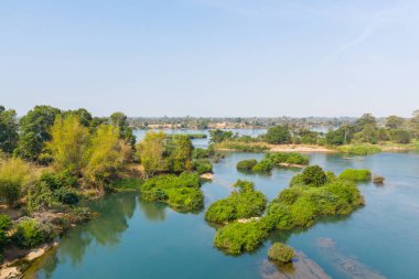 Güney Laos 'un 4000 ada bölgesindeki Mekong Nehri' nin sakin mavi sularından çok sayıda yemyeşil adacık çıkar. Parlak gün ışığı ve geniş bir gökyüzü yoğun bitki örtüsü ve temiz su kanallarıyla açık, sakin bir nehir manzarası yaratır..