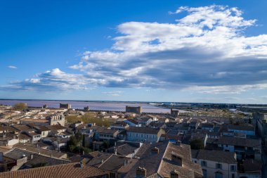 Ortaçağ surları ve pembe tuz bataklıkları olan, dağınık mavi bulutlu dramatik mavi gökyüzü altında Aigues-Mortes 'in teras çatıları üzerinde geniş bir manzara..