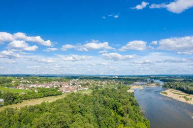 Pouilly sur Loire köyünün insansız hava aracı görüntüsü dolambaçlı Loire Nehri 'nin yanında, yemyeşil orman ve dağınık bulutlarla dolu canlı mavi gökyüzünün altında açık arazilerle çevrili. Sahne, yeni ve huzurlu bir yaz atmosferi yayıyor..