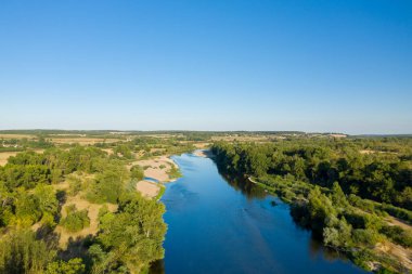 Loire Nehri 'nin geniş hava perspektifi yemyeşil ormanlarda ve açık alanlarda berrak mavi gökyüzünün altında süzülüyor. Sahne doğal kıvrımları, canlı yaprakları ve yazın kırsal bir nehir vadisinin sakin atmosferini yakalıyor..
