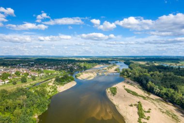 Loire Nehri 'nin kumlu sahiller, yeşil ormanlar ve dağınık bulutlarla dolu bir gökyüzünün altındaki Pouilly sur Loire köyünün kıvrımlı hava manzarası. Canlı sahne, doğal dokuları ve kırsal Fransa 'nın sakinliğini vurguluyor..