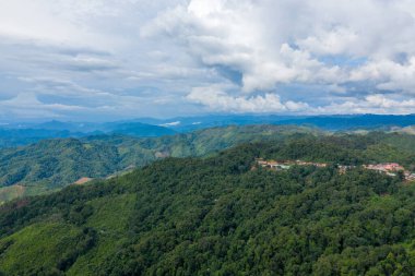 Yoğun ormanlık tepelerin arasına yerleşmiş küçük bir kırsal yerleşim yeri, geniş dağ sırtları dramatik bulutlarla dolu bir gökyüzünün altına kadar uzanıyor. Sahne, Laos 'un uzak sükunetini ve katmanlı manzarasını yakalıyor.