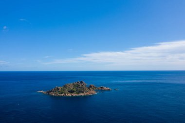 Sardunya 'nın Lotzorai yakınlarındaki engin ve berrak bir gökyüzünün altında, derin mavi Akdeniz' den yeşil bitki örtüsüyle kaplı ıssız bir kayalık ada yükselir. Parlak güneş ışığı ve yumuşak bulutlar dingin ve geniş bir deniz manzarası yaratır..