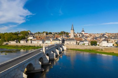 Parlak gün ışığı, La Charite sur Loire 'deki Loire Nehri' ni geçen taş köprüyü aydınlatıyor. Geleneksel evler ve nehir kenti üzerinde yükselen yüksek bir kilise kulesiyle. Sahne canlı çatılar, yemyeşil yemyeşil ve durgun mavi içerir.