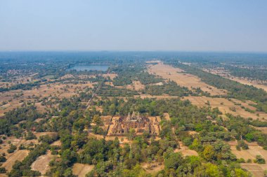 Kamboçya 'nın Angkor bölgesindeki kuru tarlalar, dağınık ağaçlar ve uzak su rezervleriyle çevrili antik Pre Rup tapınağı kompleksinin geniş hava perspektifi. Sahne, kırsal alandaki tapınakların geometrik düzenini yakalıyor.