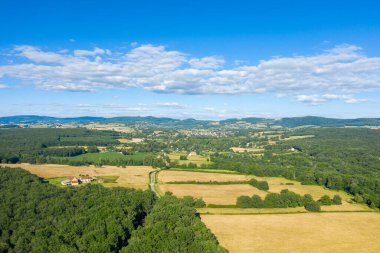Altın tarlaların, dağınık çiftlik evlerinin havadan görünüşü ve Saint-Honore-les-Bains yakınlarındaki yuvarlanan tepeler altında canlı mavi bir gökyüzünün altındaki yemyeşil ormanlık alan..