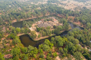 Kamboçya 'daki antik Bakong tapınağı kompleksinin yüksek açılı perspektifi dikdörtgen hendek ve yoğun yeşil ağaçlarla çevrili. Tarihi Angkor bölgesi kırsal bölgelerin ve puslu gün ışığında dağınık köy evlerinin arasına kurulmuştur..