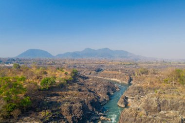 Laos 'un güneyindeki Li Phi Şelaleleri olarak da bilinen Tat Somphamit Şelaleleri' ndeki kayalık vadi ve kıvrımlı nehrin geniş hava manzarası. Kurak mevsim manzaraları seyrek ormanlar, açık taşlar ve yumuşak mavi gökyüzünün altındaki uzak tepeler..