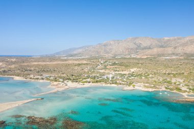Yunanistan 'ın Girit kentindeki Elafonisi plajının hava manzarasında canlı turkuaz sular, kumlu koylar ve berrak mavi bir gökyüzü altında kurak tepeler yer alıyor. Manzara güneşli, geniş ve doğal desenli..
