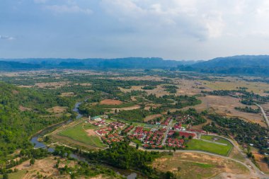 Kırmızı çatılı binaları olan planlanmış bir köy, dolambaçlı bir nehir ve açık kırsal ve uzak dağlarla çevrili yeşil tarlaların yanında yer alıyor. Manzarada bir tarım arazisi mozaiği, orman arazileri ve yumuşak toprak altında geniş bir vadi arazisi yer alıyor.