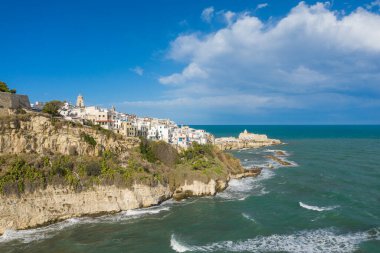 İtalya 'nın güneyindeki turkuaz Adriyatik Denizi' ne tepeden bakan engebeli kireçtaşı kayalıkların tepesinde Vieste 'nin tarihi beyazlatılmış binaları. Sahne dramatik kıyı mimarisi, dokulu kaya yüzeyleri ve geniş bir mavi gökyüzü ile tanımlanır..