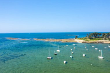 Anse de Trehennarvour, Saint Philibert 'te kayalık bir kıyı şeridi yakınlarındaki şeffaf yeşil suya demirlemiş küçük teknelerin ve yoğun çam ağaçlarının hava manzarası..
