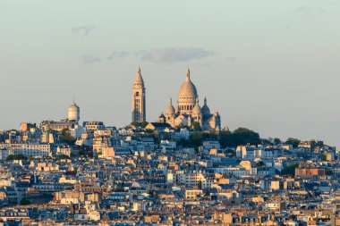 Montmartre Tepesi 'ni kaplayan Sacre Coeur Bazilikası' nın uzak manzarası, Paris 'in katmanlı çatılarıyla çevrili berrak bir gökyüzünün altında, yumuşak altın akşam ışığı altında parlayan..